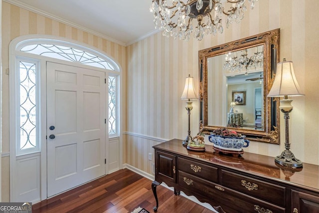 entrance foyer featuring wallpapered walls, wainscoting, dark wood-style flooring, crown molding, and a notable chandelier