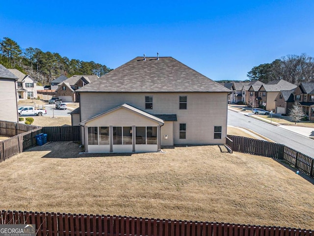 back of house with a residential view, a sunroom, a fenced backyard, and a yard