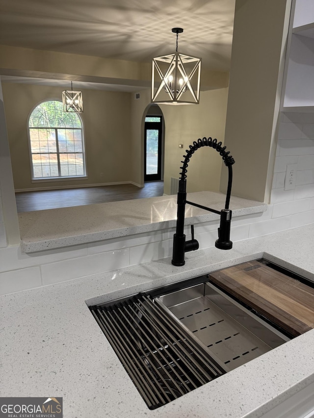 interior details with arched walkways, light stone counters, a sink, hanging light fixtures, and an inviting chandelier