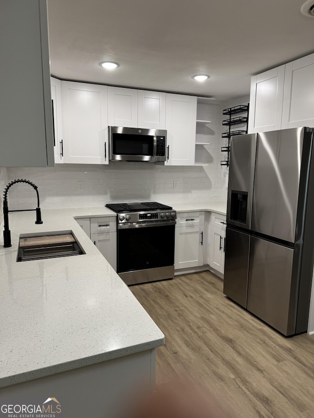 kitchen featuring appliances with stainless steel finishes, light wood-type flooring, a sink, and light stone counters