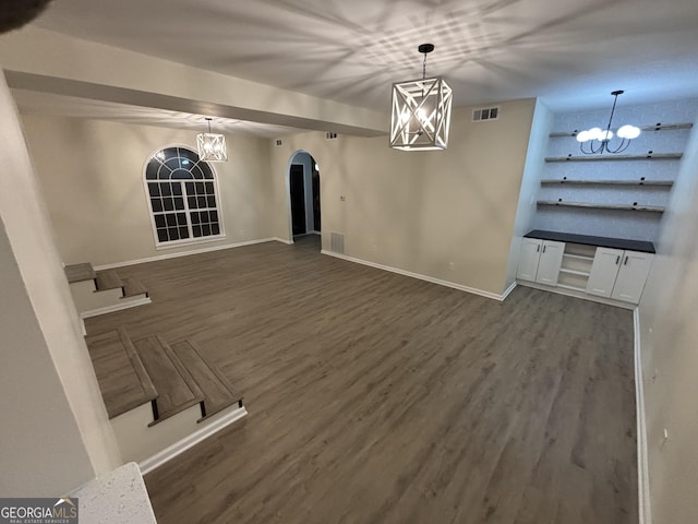 unfurnished dining area featuring dark wood-style floors, visible vents, arched walkways, and a notable chandelier