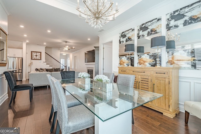 dining space featuring stairway, ornamental molding, dark wood-type flooring, a glass covered fireplace, and ceiling fan with notable chandelier