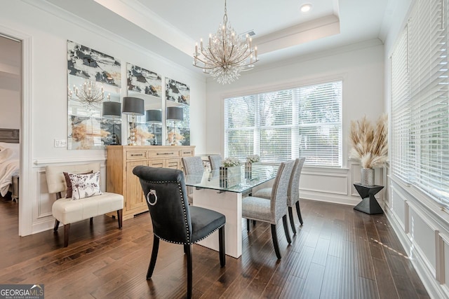 dining area featuring a decorative wall, dark wood-type flooring, ornamental molding, a notable chandelier, and a raised ceiling