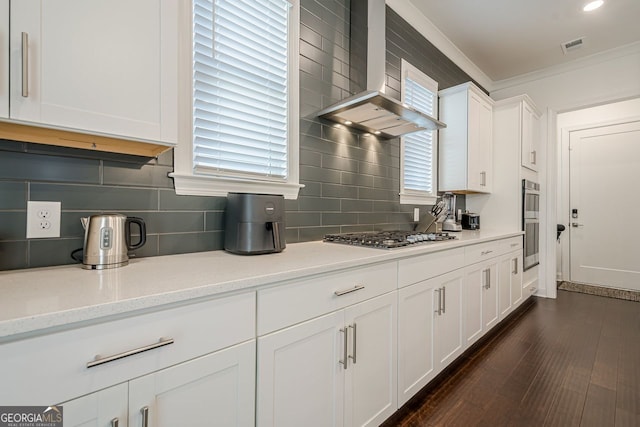 kitchen with dark wood-style floors, stainless steel appliances, wall chimney exhaust hood, crown molding, and white cabinets