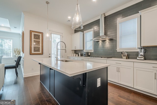 kitchen with dark wood finished floors, stovetop, a sink, crown molding, and wall chimney range hood