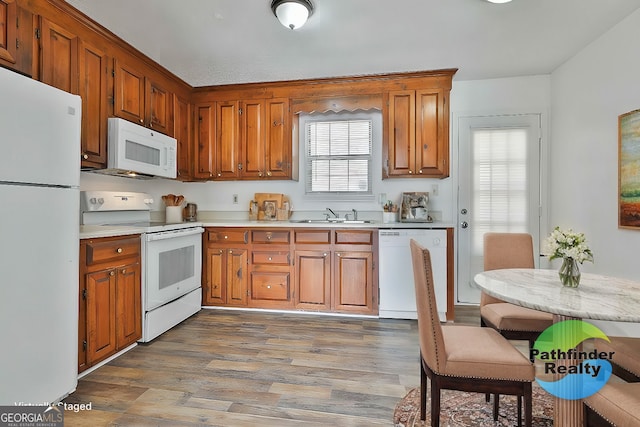 kitchen with white appliances, brown cabinetry, light wood-style flooring, light countertops, and a sink