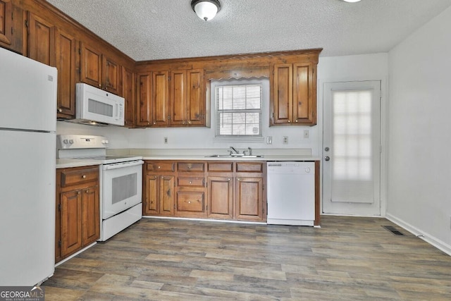 kitchen with light countertops, a sink, a textured ceiling, wood finished floors, and white appliances