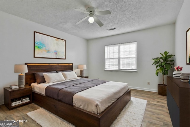 bedroom featuring baseboards, visible vents, a ceiling fan, wood finished floors, and a textured ceiling