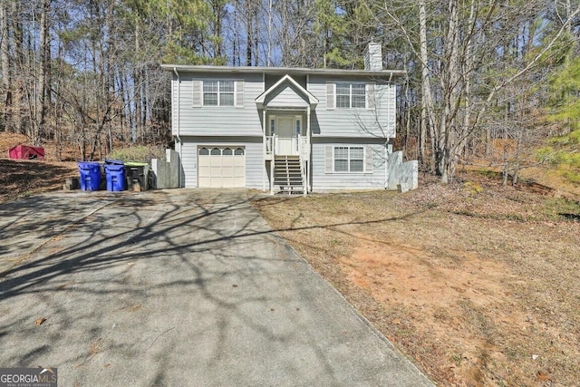 raised ranch with a garage, a chimney, and aphalt driveway