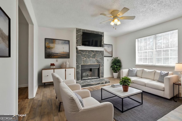 living room with ceiling fan, a fireplace, a textured ceiling, and wood finished floors