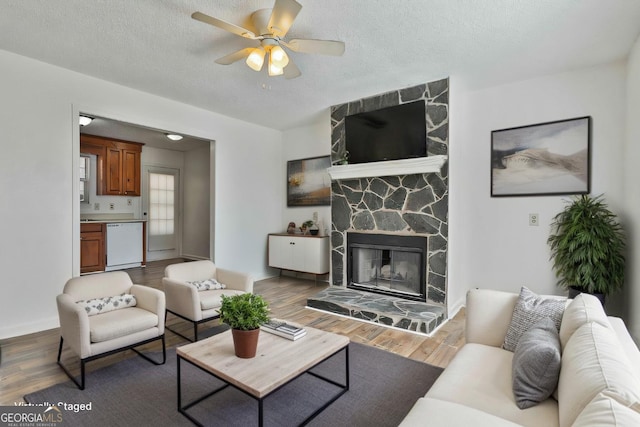 living area featuring ceiling fan, a fireplace, a textured ceiling, and wood finished floors