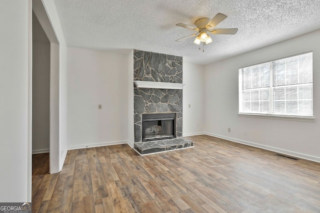 unfurnished living room with a textured ceiling, a fireplace, wood finished floors, visible vents, and a ceiling fan