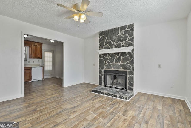 unfurnished living room with a fireplace, a ceiling fan, a textured ceiling, wood finished floors, and baseboards