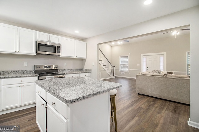 kitchen featuring a center island, dark wood finished floors, stainless steel appliances, open floor plan, and white cabinetry