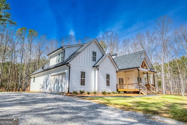 view of side of property with ceiling fan, covered porch, a yard, board and batten siding, and gravel driveway