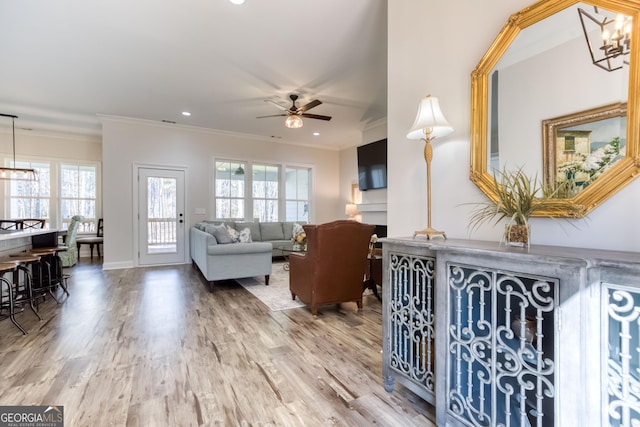 living area featuring ceiling fan with notable chandelier, baseboards, wood finished floors, and crown molding