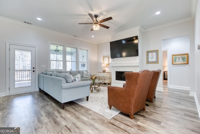 living area with light wood-type flooring, ornamental molding, a fireplace, and visible vents