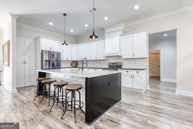 kitchen with an island with sink, custom range hood, appliances with stainless steel finishes, crown molding, and a sink