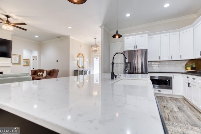 kitchen featuring a sink, open floor plan, appliances with stainless steel finishes, ornamental molding, and decorative backsplash