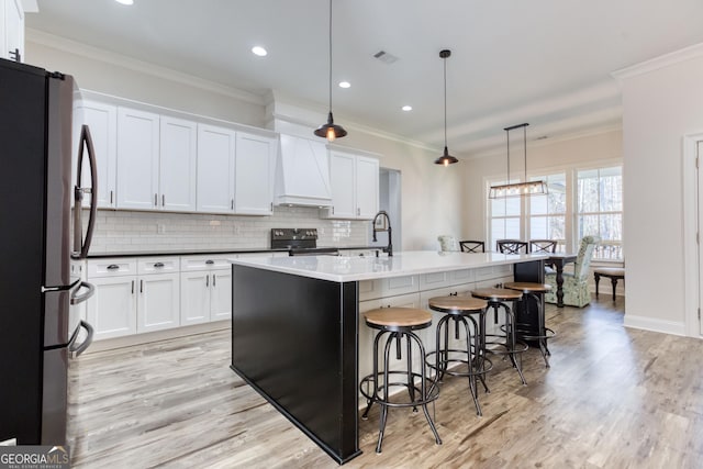 kitchen with custom exhaust hood, stainless steel appliances, tasteful backsplash, light wood-style flooring, and ornamental molding