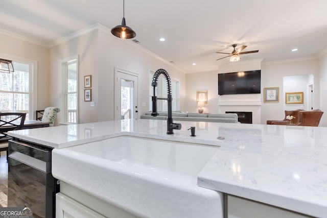 kitchen featuring light stone countertops, a fireplace, ornamental molding, and a sink