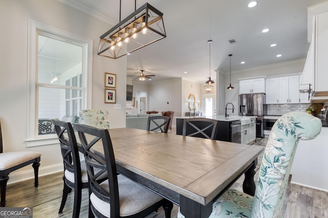 dining room with ornamental molding, light wood-style flooring, baseboards, and a ceiling fan