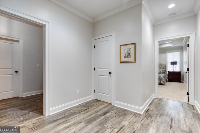 corridor featuring baseboards, light wood-style flooring, and crown molding