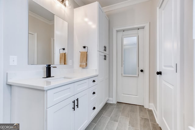 bathroom with baseboards, wood finish floors, crown molding, and vanity