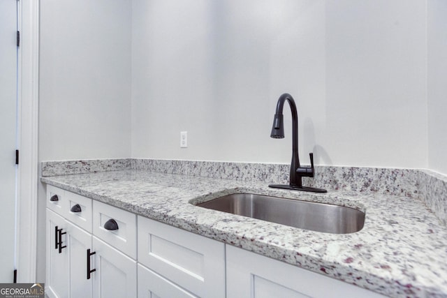 kitchen with white cabinets, a sink, and light stone countertops