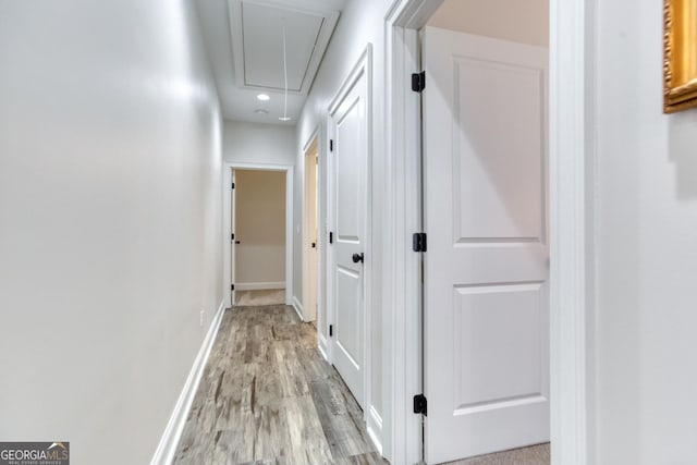 hall featuring attic access, light wood-style flooring, and baseboards