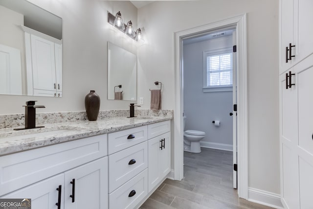 bathroom featuring baseboards, a sink, toilet, and double vanity