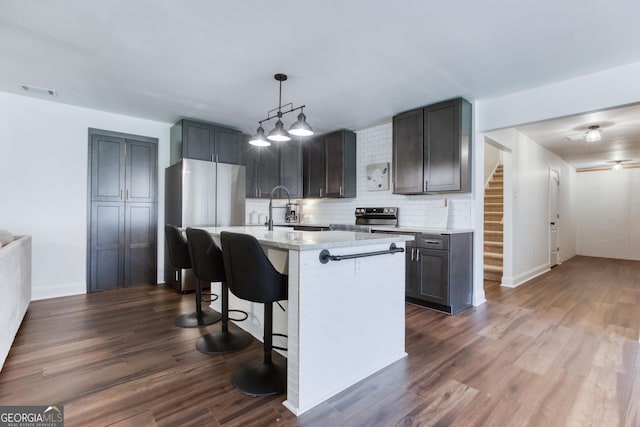 kitchen featuring appliances with stainless steel finishes, dark wood-type flooring, a sink, a kitchen bar, and backsplash