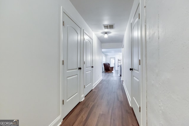 corridor with dark wood-style flooring, visible vents, and baseboards