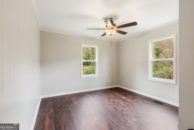 empty room featuring ceiling fan, dark wood-type flooring, visible vents, baseboards, and crown molding