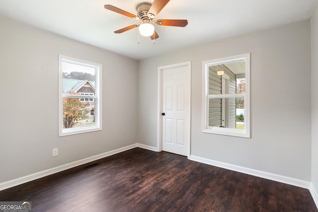 empty room with a ceiling fan, dark wood finished floors, visible vents, and baseboards