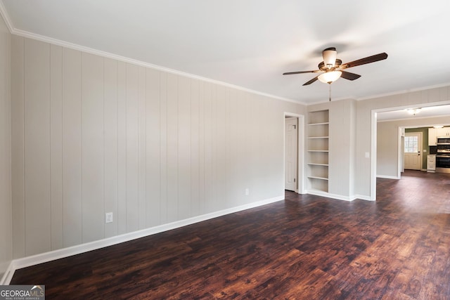 empty room featuring built in shelves, a ceiling fan, baseboards, dark wood finished floors, and crown molding