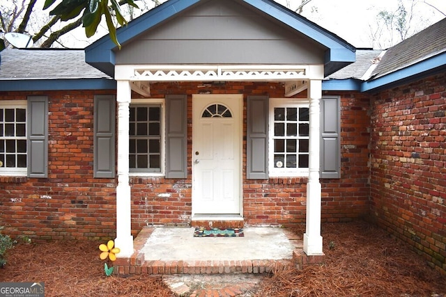 entrance to property with a shingled roof and brick siding