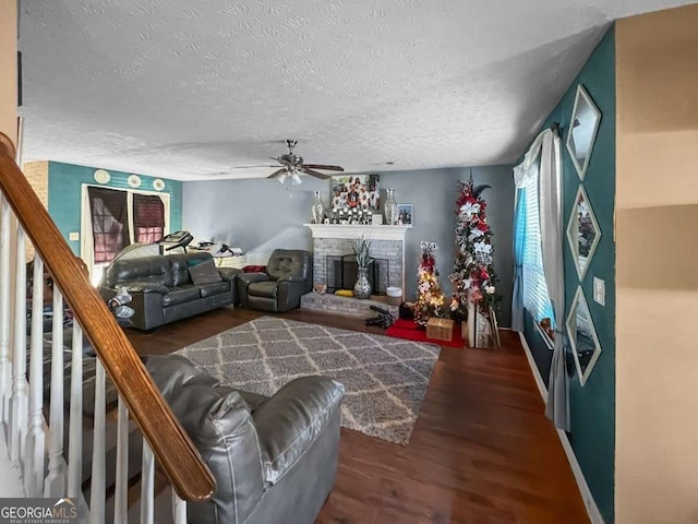 living room featuring a textured ceiling, a fireplace, wood finished floors, a ceiling fan, and stairs