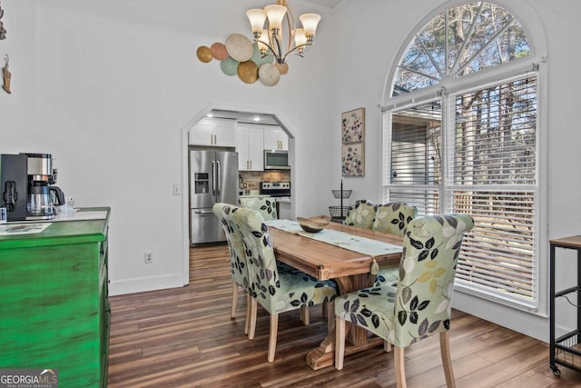 dining room with baseboards, a notable chandelier, arched walkways, and wood finished floors