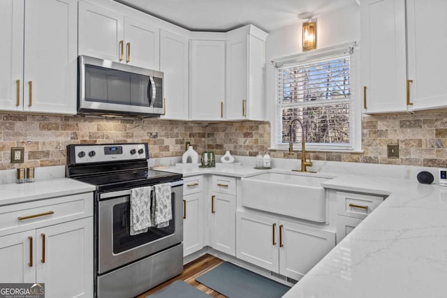 kitchen with light stone counters, backsplash, appliances with stainless steel finishes, white cabinets, and a sink