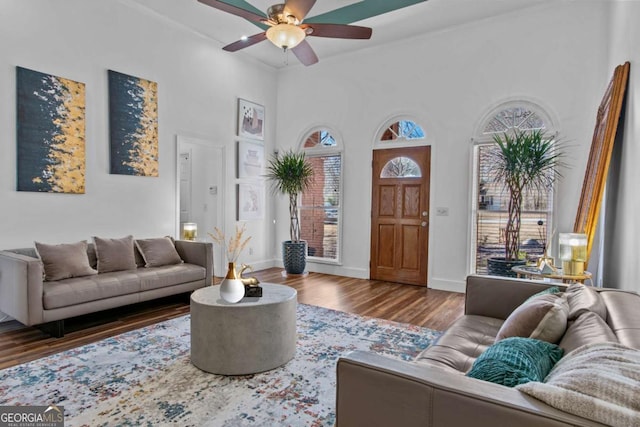 living area featuring a towering ceiling, wood finished floors, a ceiling fan, and baseboards