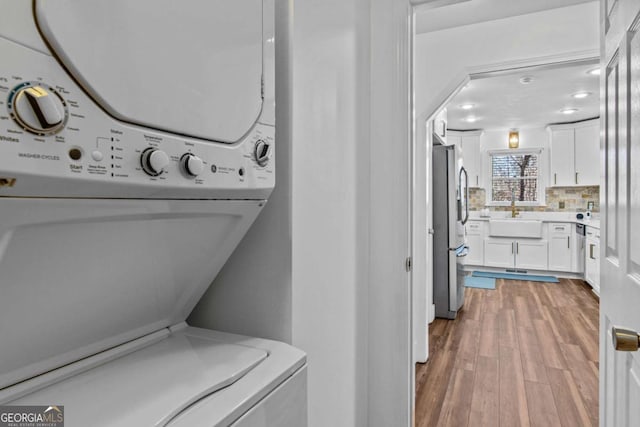 laundry room with laundry area, stacked washer / dryer, a sink, and light wood-style floors