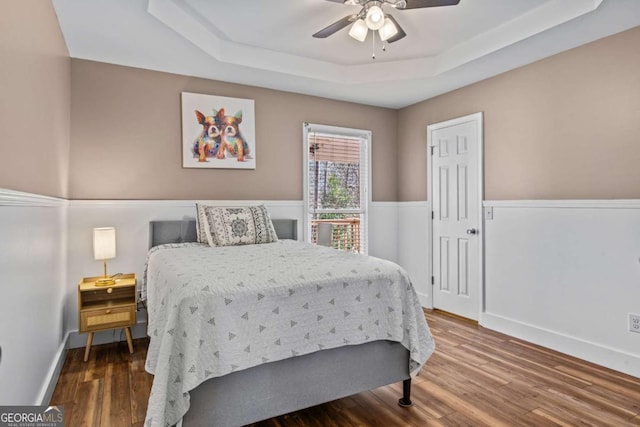 bedroom with ceiling fan, a tray ceiling, wood finished floors, and baseboards