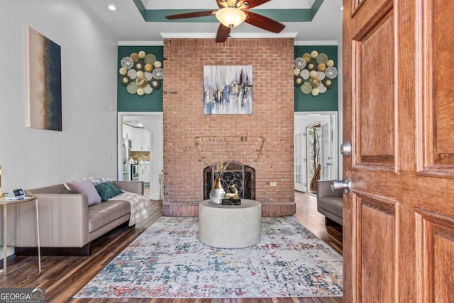 living area featuring a brick fireplace, ceiling fan, dark wood-style floors, and crown molding