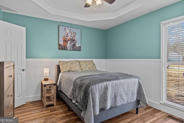 bedroom with visible vents, baseboards, a ceiling fan, wood finished floors, and a tray ceiling