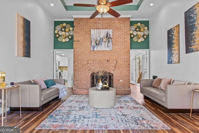 living area featuring a brick fireplace, a ceiling fan, crown molding, and wood finished floors