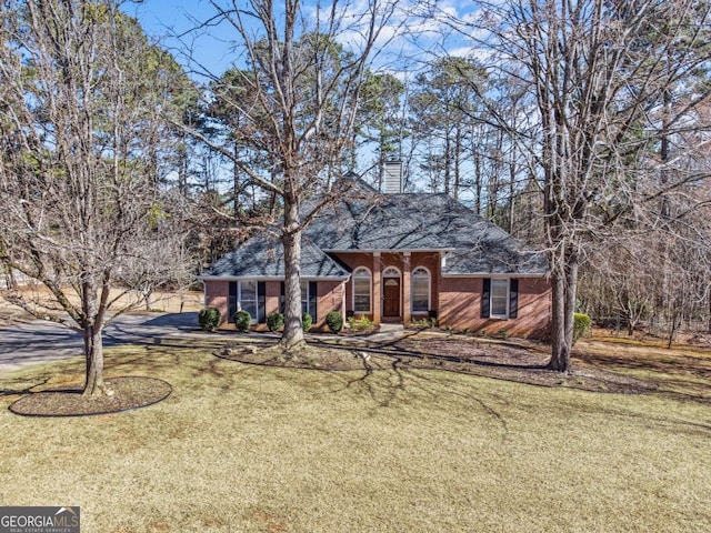 view of front facade with driveway, a front yard, a chimney, and brick siding