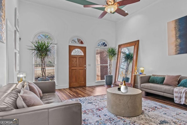 living area featuring a towering ceiling, baseboards, a ceiling fan, and wood finished floors