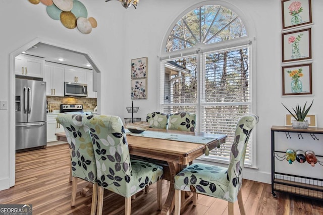 dining space featuring arched walkways, baseboards, light wood-style flooring, and a high ceiling