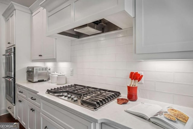 kitchen featuring stainless steel appliances, white cabinetry, light countertops, custom exhaust hood, and tasteful backsplash